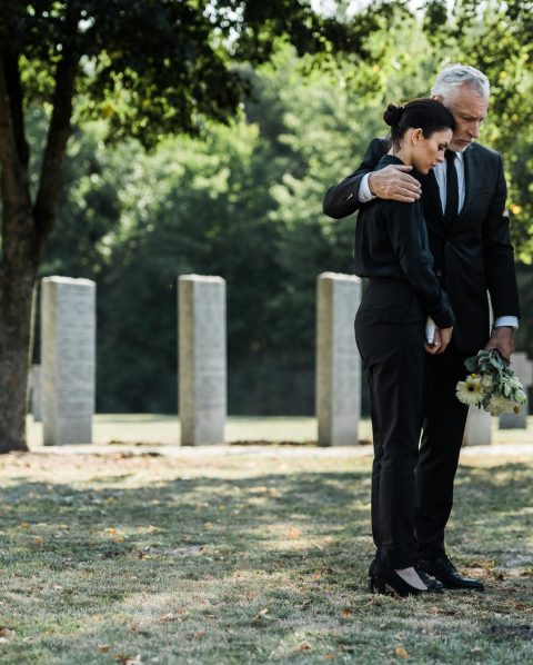 upset man hugging frustrated woman in cemetery